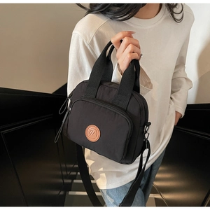 Nahaufnahme der schwarzen Nylon-Umhängetasche mit rundem Logo-Patch und Reißverschluss