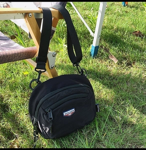 Dettaglio della borsa a tracolla in nylon nero con cerniere su una sedia di legno