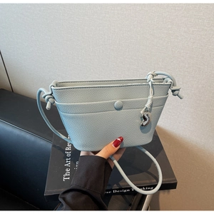 Détail du sac à bandoulière en cuir grainé bleu clair avec breloque cœur et bandoulière nouée