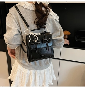 Gros plan du sac à dos en cuir verni noir avec nœuds et pendentif en perles