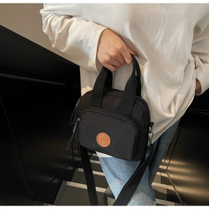 Detail einer schwarzen Nylon-Handtasche mit braunem Logo-Patch und Reißverschluss