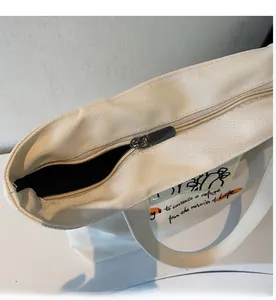Detail showing the smooth black metal zipper closure and fabric texture of the canvas tote bag