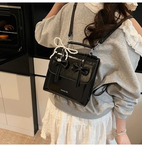 Détail d'un sac à dos en cuir verni noir avec nœuds décoratifs et charm en perles
