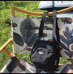 Dettaglio di una borsa a tracolla in nylon nero con logo a scudo su una sedia da campeggio