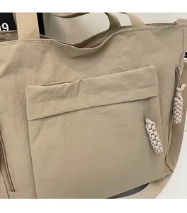 Detail of khaki nylon tote bag showing wrinkled fabric texture and braided zipper puller