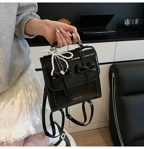 Détail d'un sac à dos en cuir verni noir avec nœuds et pendentif en perles