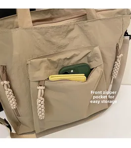 Close-up of khaki nylon tote with front zipper pocket and woven puller detailing