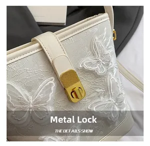 Détail du fermoir rotatif en métal doré et de la broderie sur le sac seau de couleur crème
