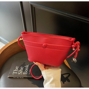 Détail du sac bandoulière en cuir rouge avec sangle nouée et pendentif cœur en métal