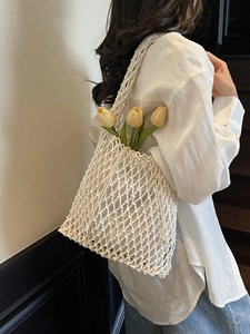 White macrame woven bucket bag with floral accent shown in a minimalist lifestyle setting
