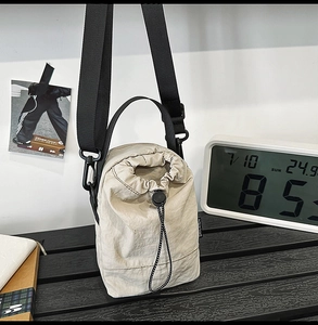 Detail of beige nylon drawstring bucket bag showing adjustable cord and fabric side label