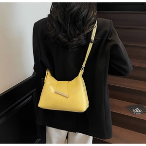 Detail einer glänzenden gelben Hobo-Bag mit goldener Schnalle über einem schwarzen Sakko