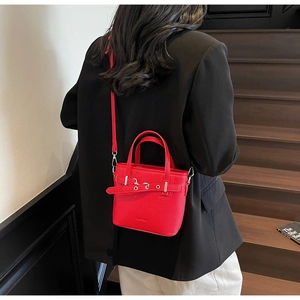 Dettaglio della mini borsa in pelle rossa con fibbia sulla spalla di un modello