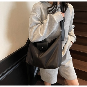 Detail of a large Oxford cloth tote bag with leather flap shown on a model on stairs