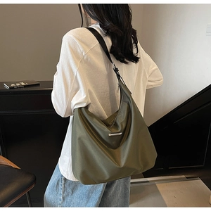Detail of olive green nylon tote bag with silver metal trim shown in daily commuting use
