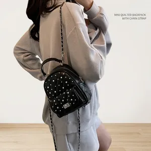 Detail of black quilted mini backpack featuring silver studs and metal chain straps