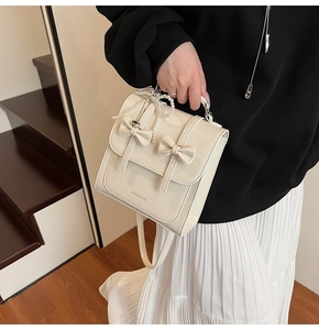 Détail d'un sac à dos crème avec nœuds élégants et pendentif en perles raffiné