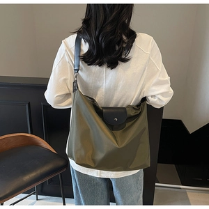Detail of olive green nylon tote bag featuring a leather flap and metal snap button