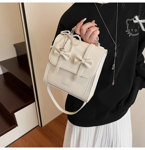 Détail d'un sac à main crème brillant avec des nœuds décoratifs et un pendentif perle