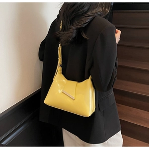 Glänzende gelbe Schultertasche aus Lackleder mit Metallschnalle am Arm des Models
