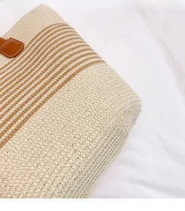 Gros plan d'un sac cabas en paille tissé avec rayures brunes et base de poignée en cuir