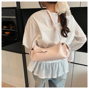 Close-up of light pink leather crescent bag with side pockets on a model in a modern bakery