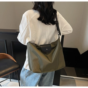 Detail of army green nylon tote bag with black leather flap and adjustable strap on model