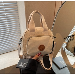 Detailaufnahme der cremefarbenen Mini-Tragetasche aus Nylon mit Logo und Griffen