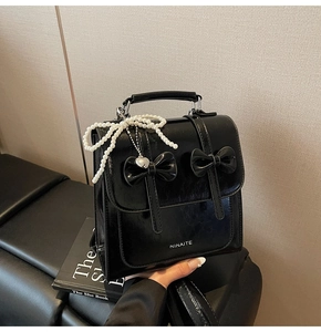 Détail du sac à dos en cuir noir avec nœuds décoratifs et pendentif cœur perlé