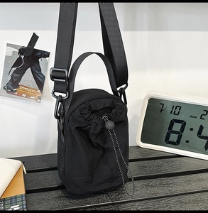 Detail of black nylon mini drawstring crossbody bag with adjustable wide webbed shoulder strap