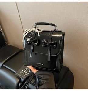 Gros plan d'un sac à main en cuir verni noir avec nœuds et breloques en perles