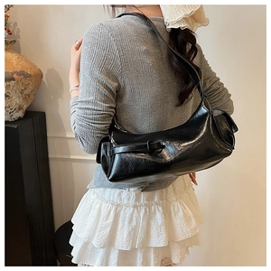 Detail of glossy black shoulder bag showing curved structure and decorative side pockets
