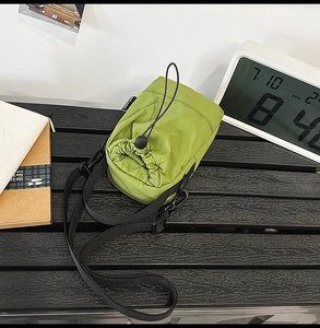 Detail view of the grass green nylon drawstring crossbody bag on a textured wooden surface