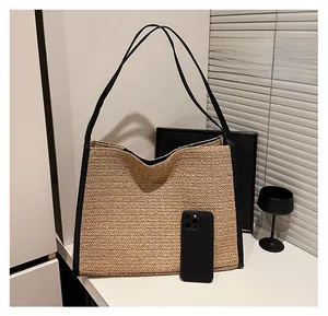 Détail d'un grand sac cabas en paille avec anses en cuir noir et téléphone pour comparaison