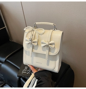 Détail d'un sac à dos en cuir blanc crème avec nœuds élégants et breloque en perles