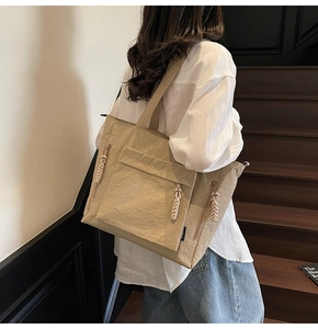 Detail of khaki nylon tote bag with side zippers and woven pulls worn on shoulder