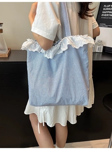Blue striped canvas tote bag with white lace trim shown on a shoulder in a cafe