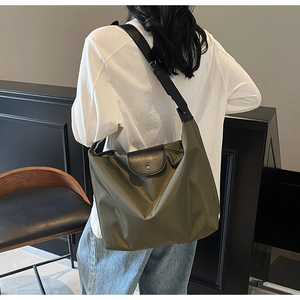 Detail of olive green nylon tote bag with black leather strap on a model's shoulder