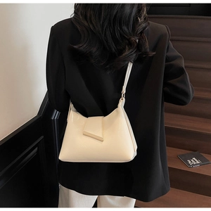 Schicke cremefarbene Leder-Schultertasche mit Goldleiste am Model auf Holztreppen