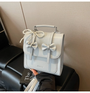 Détail d'un sac à dos en cuir bleu clair avec nœuds décoratifs et breloque cœur en perles