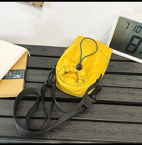 Close-up of yellow nylon crossbody bag with drawstring closure on dark wooden bench