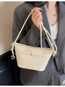 Sac seau minimaliste en cuir beige avec pendentif cœur sur mannequin en blazer gris