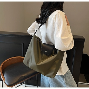 Olive green nylon tote bag with black leather flap shown worn on shoulder by a model