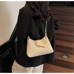 Detail einer glänzenden cremefarbenen Hobo-Tasche mit Metallschnalle am Gurt