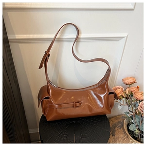 Close-up of brown glossy leather crescent bag featuring side pockets and metal zipper