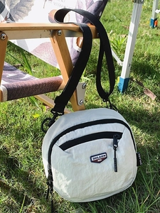 Piccola borsa a tracolla minimalista in nylon beige su sedia in legno in ambiente esterno