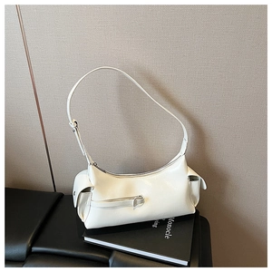 Close-up of a white glossy crescent shoulder bag with side pockets on a book