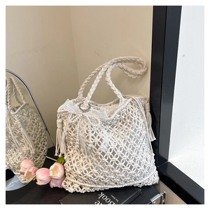 Détail du sac en paille blanche avec nœud en dentelle, perle et pompons sur une surface noire