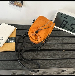 Detail of orange drawstring bucket bag made of water-resistant nylon with black strap
