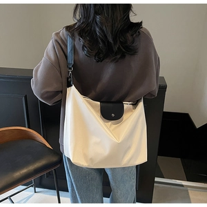 Detail view of large cream and black tote bag with silver buckle worn on shoulder